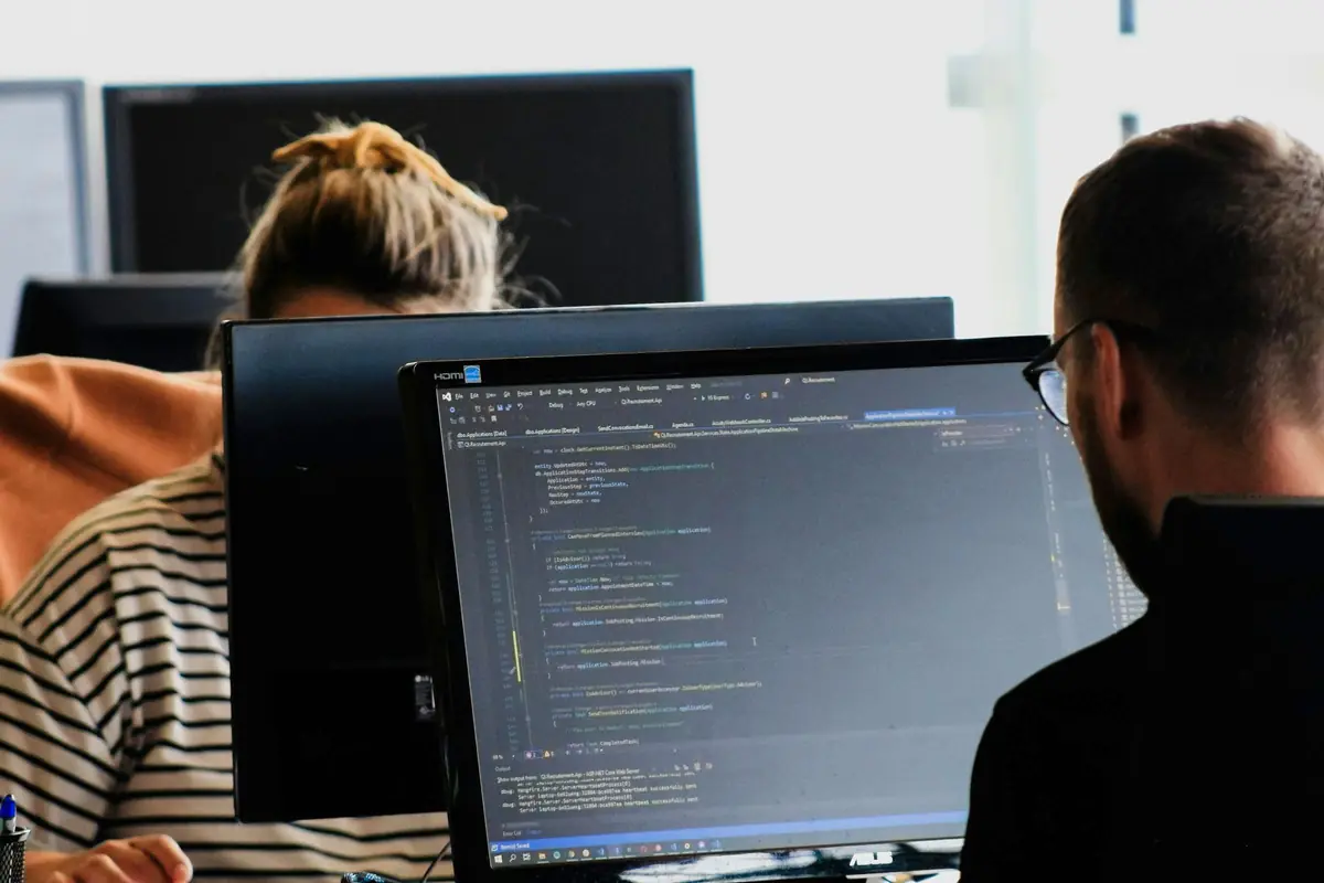 Two engineers working together at a pair of monitors.